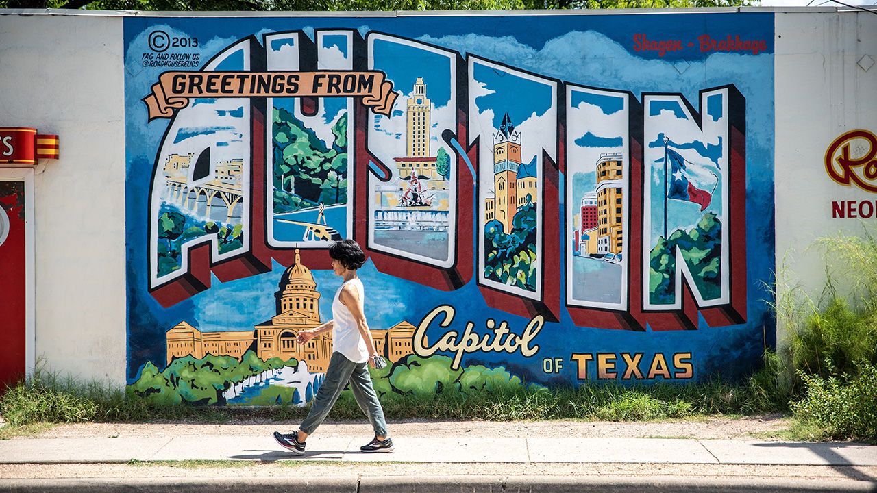 A woman walks by the "Greetings From Austin Texas" mural in Austin, Texas