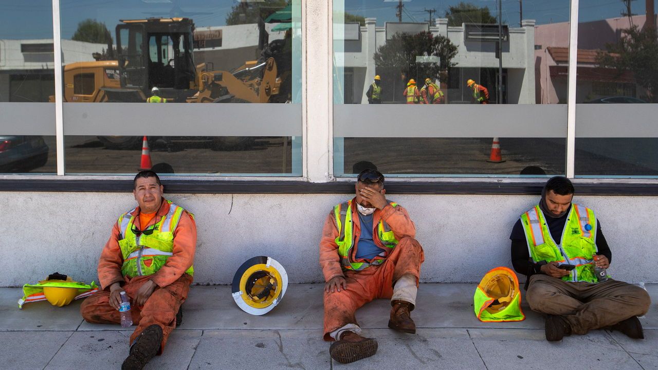 LA City street services workers take a break in the shade of a nearby storefront on a hot day