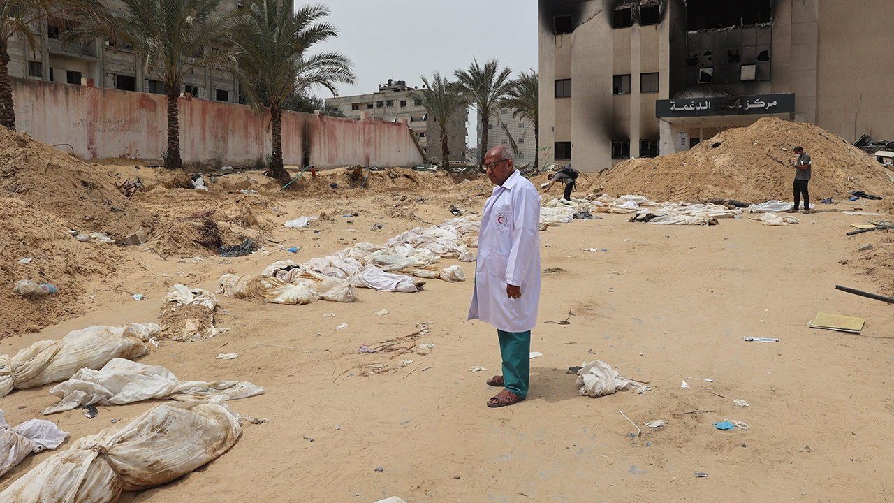 A doctor stands near bodies lined up for identification after they were unearthed from a mass grave found in the Nasser Medical Complex.