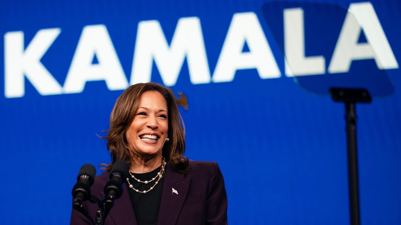 Vice President Kamala Harris stands in front of a sign with 'Kamala'.