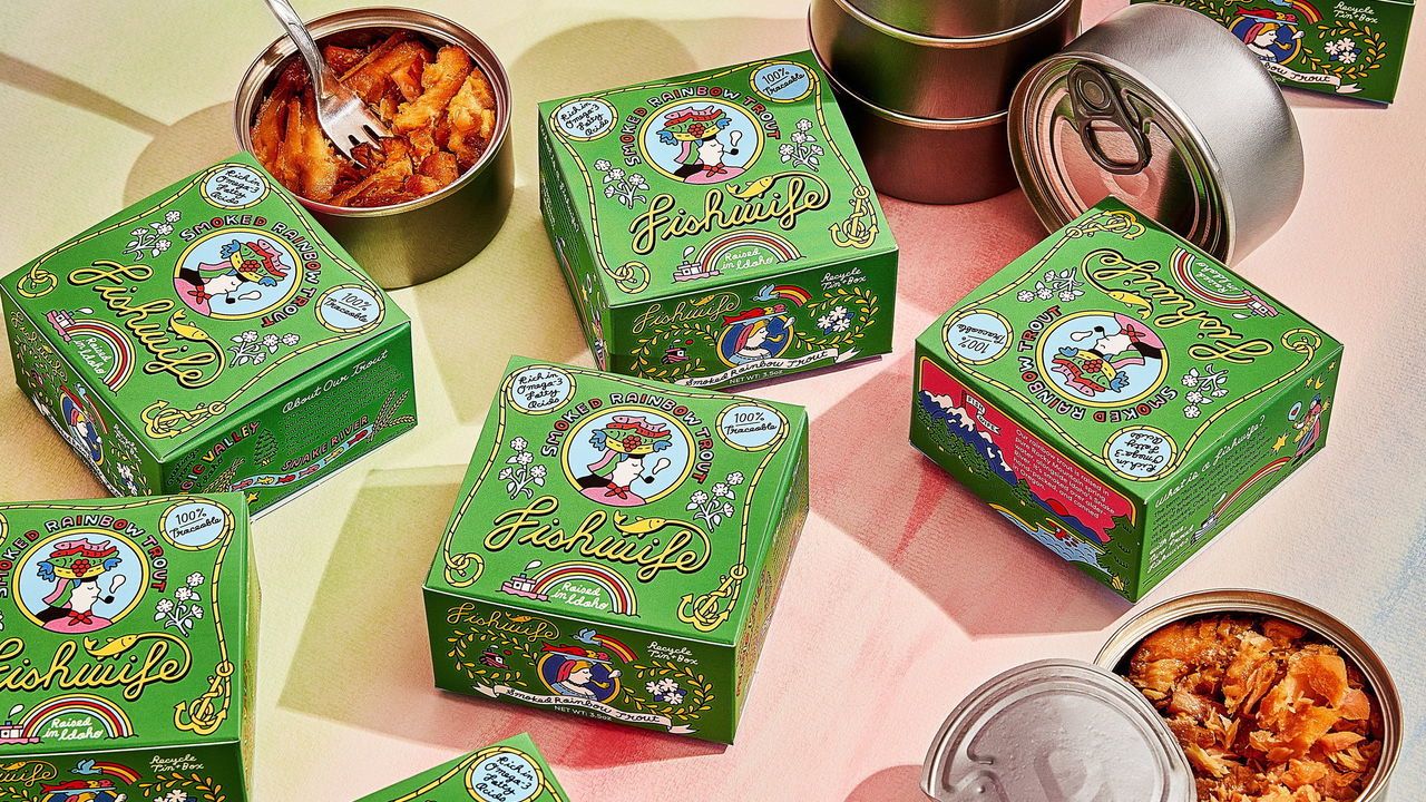 Colourful packaging of 'Fishwife Tinned Seafood Co' produce. Two opens tins of Smoked Rainbow Trout surrounded by green boxes.